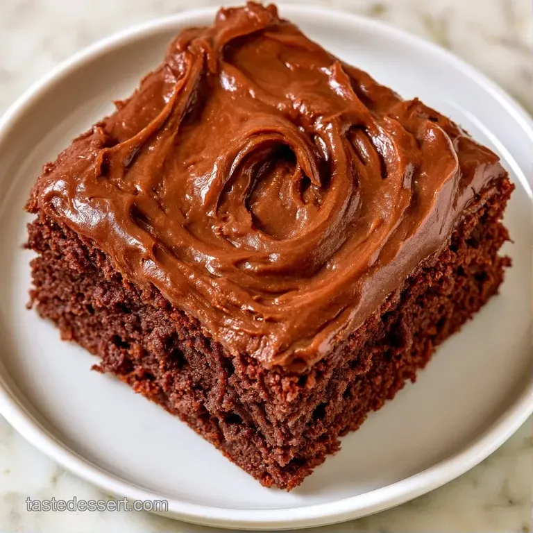 A neat square of moist dark cake on a white plate, drizzled with glossy chocolate sauce and a fresh mint leaf.