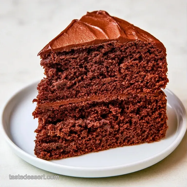 A slice of dark, moist cake on a white plate, topped with a dollop of cream and a single fresh raspberry.